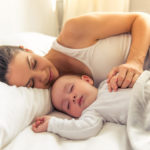 Młoda kobieta śpiąca w łóżku z niemowlęciem - zdrowy-sen.eu