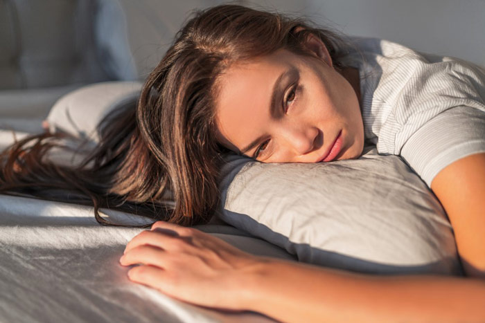 Młoda, zmęczona kobieta (z głową na poduszce), cierpiąca na wzmożoną senność w ciągu dnia - zdrowy-sen.eu