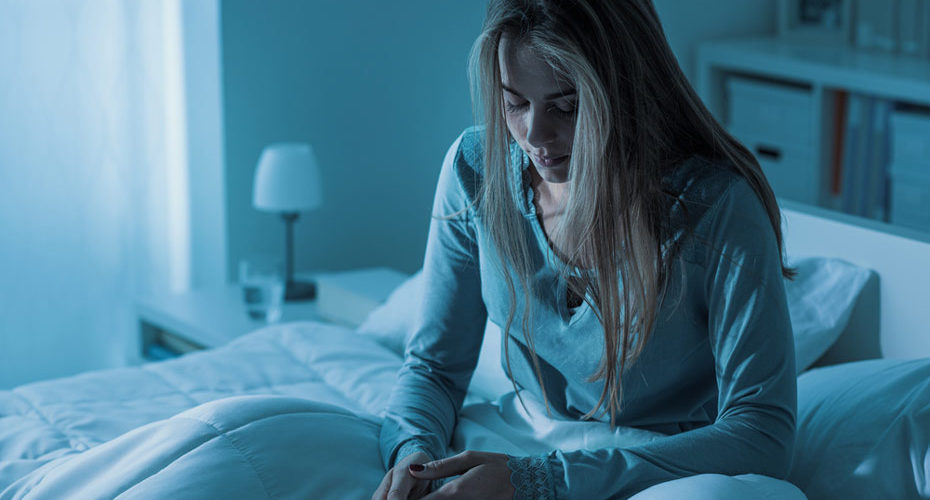 Młoda kobieta z zaburzeniami snu siedząca na łóżku w swojej sypialni – zdrowy-sen.eu