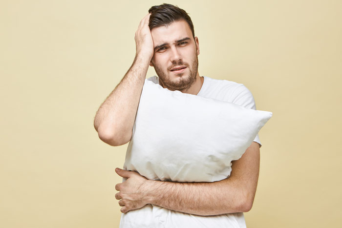Mężczyzna z bólem głowy po nieudanym spaniu z poduszką w ręku – zdrowy-sen.eu